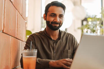 Middle aged professional Indian businessman enjoying beverage while working on laptop in cafe