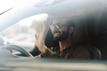 Happy businessman waving while driving modern car