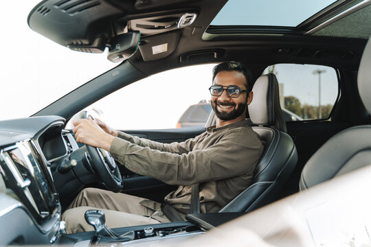Happy Indian businessman smiling while driving modern car looking at camera