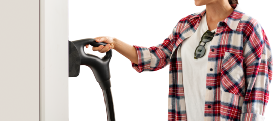 Isolated female person in red plaid shirt with electric plug in her hand on electric vehicle  charging station.