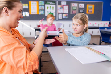 Practicing sign language, female teacher and student in school classroom, smiling together