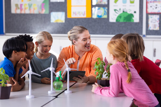 In school, female teacher with tablet, engaging diverse students with wind turbines and plants - Powered by Adobe
