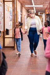 Walking in school hallway, female teacher holding hands with two diverse students, smiling