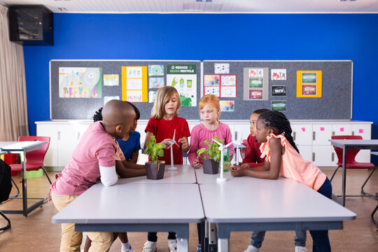 In school, diverse children examining plants and wind turbine models in classroom