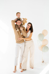 Young mother and father are holding son and teddy bear against a backdrop of balloons