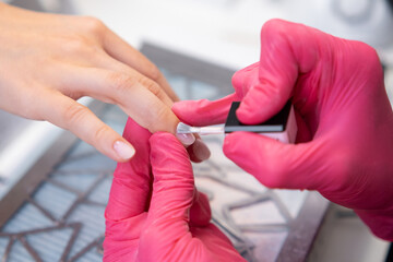 A professional manicurist is applying gel polish to a woman nails during a manicure session.
