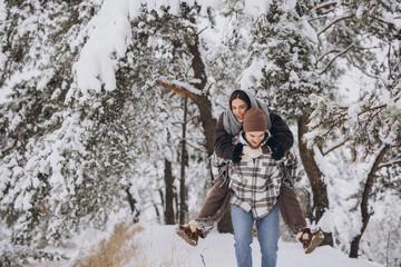A young happy and loving couple is having fun in a snowy forest in winter.