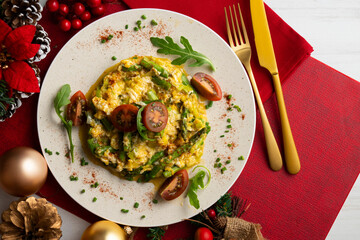 Scrambled organic chicken eggs with green asparagus and tomato. Top view table with Christmas decoration.