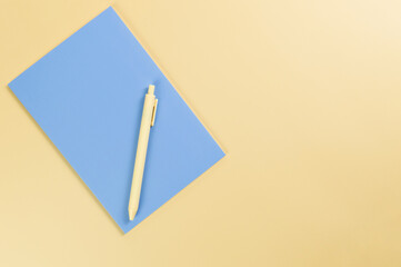 Top view of blue notebook, yellow pen on yellow background. School, office wallpaper. Flat lay, copy space.