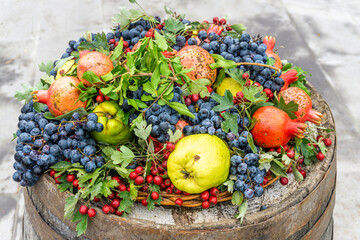 Black grapes, pomegranates, quince and branches with leaves lie on an old oak barrel