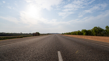 Road with red dirt around it in the middle of nowhere, Australia, blue cloudy sky, 