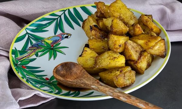 Ananas r&ocirc;ti au miel, rhum et vanille, dessert antillais pr&eacute;sent&eacute; dans un plat d&eacute;cor&eacute; d&rsquo;un perroquet en feuilles de palme, avec une cuill&egrave;re en bois et un torchon rose - cuisine cr&eacute;ole