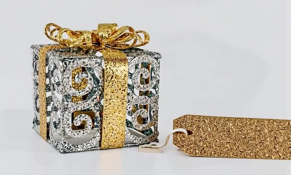 Zoom sur un paquet cadeau m&eacute;tallique or et argent avec une &eacute;tiquette dor&eacute;e sur fond blanc, parfait pour les f&ecirc;tes de fin d'ann&eacute;e comme No&euml;l et le Nouvel An