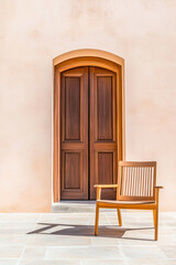 A wooden chair placed in front of a stylish door against a soft peach wall during daylight