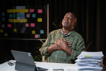 Black male entrepreneur holding hands on chest feeling gratitude working late in office