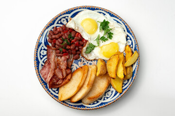 Delicious breakfast plate featuring eggs, beans, bacon, and potato wedges served on a decorative dish