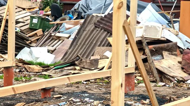 A cluttered scene of construction debris, including wood, metal sheets, and various discarded materials in an outdoor area.
