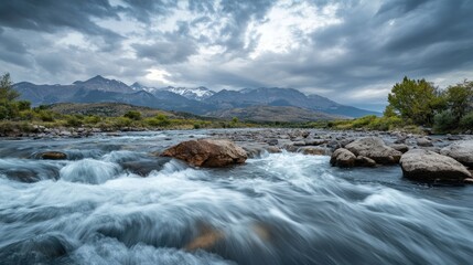 A serene river flows through a mountainous landscape under a dramatic sky.