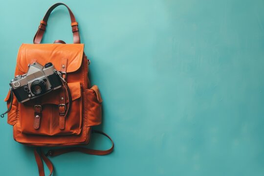 A vintage camera rests atop a stylish orange backpack against a vibrant turquoise background