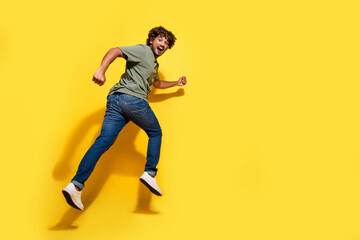 Fototapeta na wymiar Full size photo of good mood guy dressed khaki t-shirt jeans running away on sale to empty space isolated on yellow color background