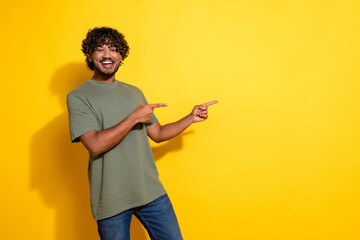 Photo of funky cheerful guy with curly hairstyle dressed khaki shirt indicating at offer empty space isolated on yellow color background