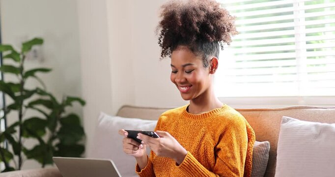 Portrait of stylish Happy african american woman in afro hair using phone on sofa 
