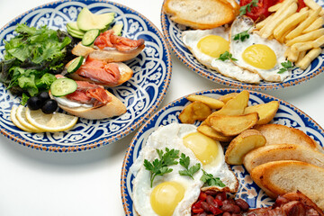 Traditional breakfast plates featuring eggs, sausages, and various accompaniments arranged artistically on a white background