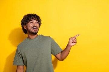 Photo of positive guy with curly hairstyle dressed khaki shirt indicating look at logo empty space isolated on yellow color background