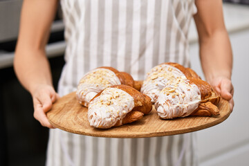 female baker holding wooden tray with freshly baked crispy golden croissants
