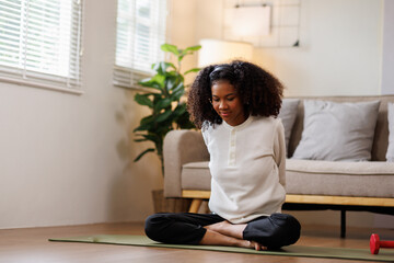 A curly African American woman in activewear practices yoga in a serene living room Meditating at Home with Headphones setting.
