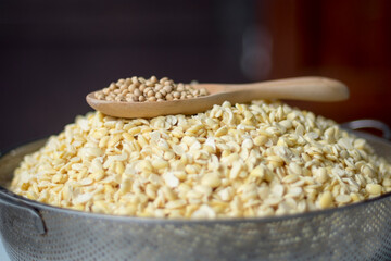 Soy beans in stainless steel sieve(prepare boiling for making tempeh and soymilk) and dry in wooden spoon on top of soy beans close up selective focus and blur blackground.