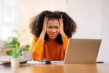 Portrait of sad upset woman feeling bad unwell with unhappy emotions holding hands on temples suffering from head ache sitting laptop desk. Health care concept
