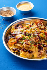Loaded Fries Nachos with Kimchi, Chicken, Cheese, Sauce, Mayonnaise dip, sesame seeds and green onion served in plate isolated on blue background closeup side view of unhealthy fast food