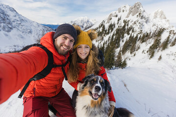 Hiker couple with a dog takes a selfie from a snowy landscape in the winter mountains