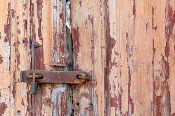 Old rusty lock on a traditional wooden door. A close-up view of a closed door. The wooden door is locked. There is a rough lock on the door.