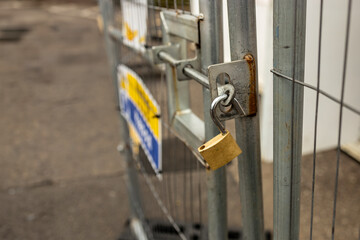 Open unlocked brass padlock bolt on a metal construction site gate with site office container in...