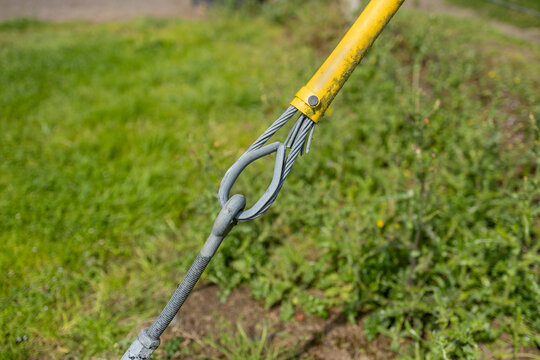 Close-up of a steel wire guy rope with yellow plastic protective cover securing a timber utility electricity transmission line telegraph pole to ground anchor bolt