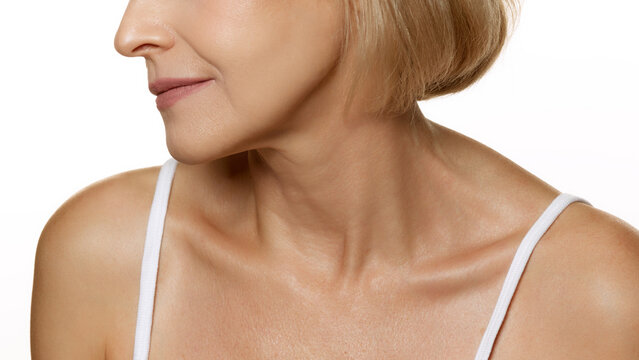 Profile view of smiling woman, showcasing natural lips and fine lines with glowing skin against white studio background. Concept of beauty, wellness, cosmetology, anti-aging products. Ad