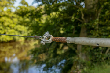 Steel wire rope cable zip line across river secured to u-bolt end assembly background of tree lined banks
