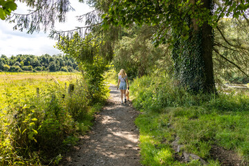 Woman wearing t-shirt, shorts, trainers walking dog on countryside footpath summers day
