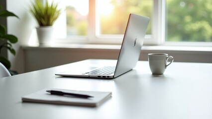 A minimalist workspace featuring a sleek laptop, a notebook with a pen, a coffee cup, and a potted plant on a white desk, set against a backdrop of large windows with soft, natural light.