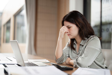 Obraz premium Stressed Business Woman Working at Desk with Laptop and Documents in Modern Office Environment