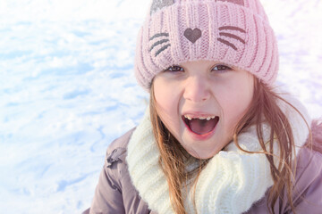 Fototapeta premium Cheerful young girl playing in the snow during winter in a cozy hat and scarf