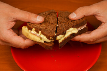 Close-up of man eating sandwich. Close-up image of a male cooking and holding sandwich. Food. Tasty sandwich. Hands holding sandwich with ham, bacon, cheese, lettuce, tomatoes.