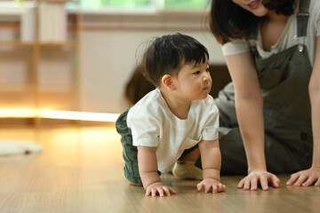 Fototapeta premium Mother watching her cute baby boy crawling on floor. Childhood and development concept