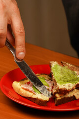 Close-up image of a male cooking and holding sandwich. Food. Tasty sandwich. Opened sandwich. Hands holding sandwich with ham, bacon, cheese, lettuce, tomatoes. Close-up of man eating sandwich.