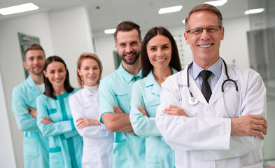 Close-up of a smiling team of healthcare professionals, including doctors and nurses in lab coats and scrubs, standing confidently in a hospital hallway. Concepts of medical care, teamwork, and trust