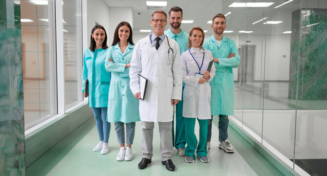 A team of smiling medical professionals in lab coats and scrubs stand confidently in a modern hospital hallway, conveying unity, expertise, and trust. Ideal for healthcare and teamwork concepts.