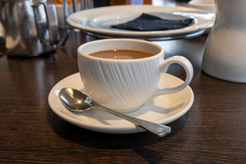 Coffee white cup and saucer, teaspoon, and milk jug on restaurant table