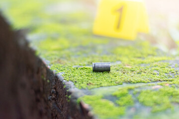 Pistol bullet shell and blurred number 1 on yellow paper on cement floor which has bright green...
